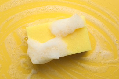 Photo of Sponge with foam on yellow background, top view