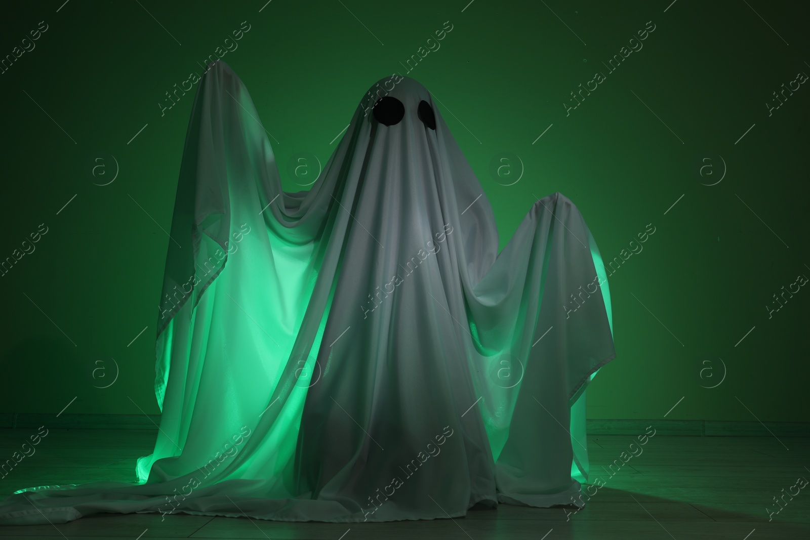 Photo of Creepy ghost. Woman covered with sheet in green light