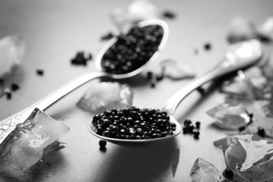 Photo of Metal spoons with black caviar and ice cubes on grey background