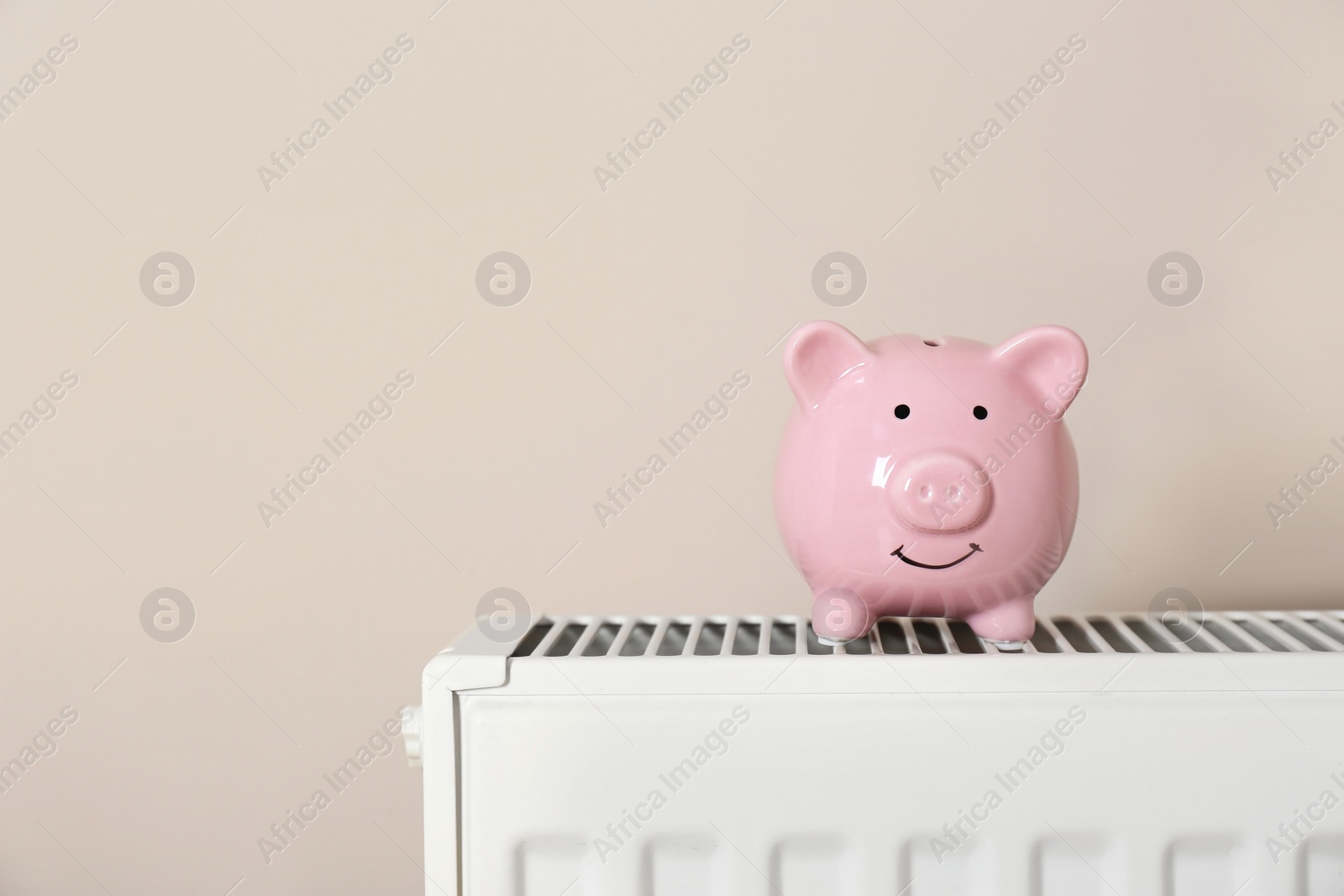 Photo of Piggy bank on heating radiator against light background. Space for text