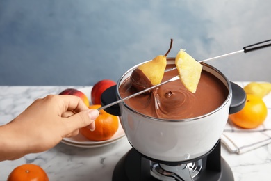 Photo of Friends dipping fruits into pot with chocolate fondue on table, closeup