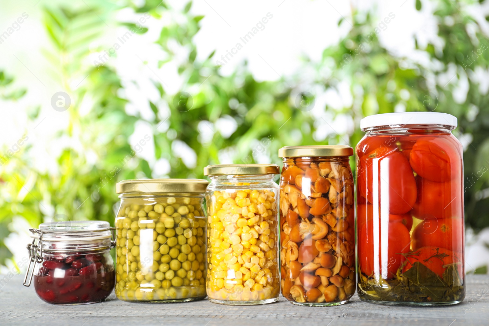 Photo of Glass jars of different pickled vegetables on wooden table