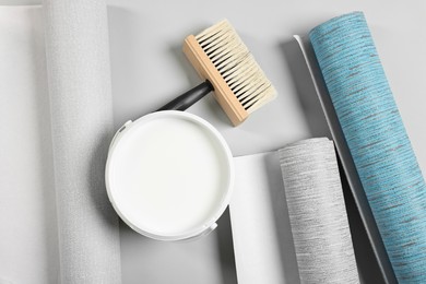 Photo of Different wallpaper rolls, brush and bucket with glue on light background, flat lay