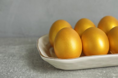 Photo of Shiny golden eggs on light grey table, closeup. Space for text