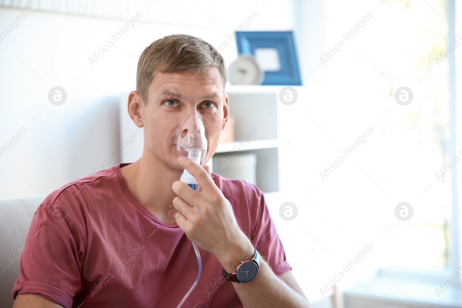 Photo of Young man using asthma machine indoors. Space for text