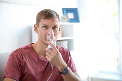 Photo of Young man using asthma machine indoors. Space for text