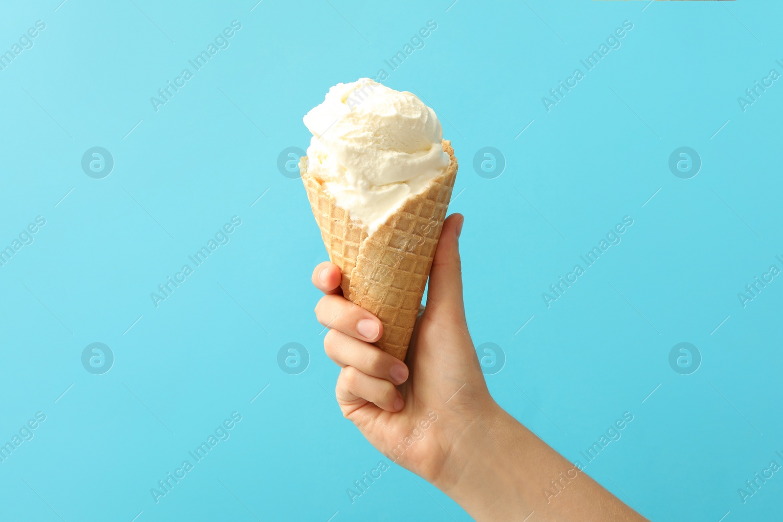 Photo of Woman holding waffle cone with delicious ice cream on light blue background, closeup