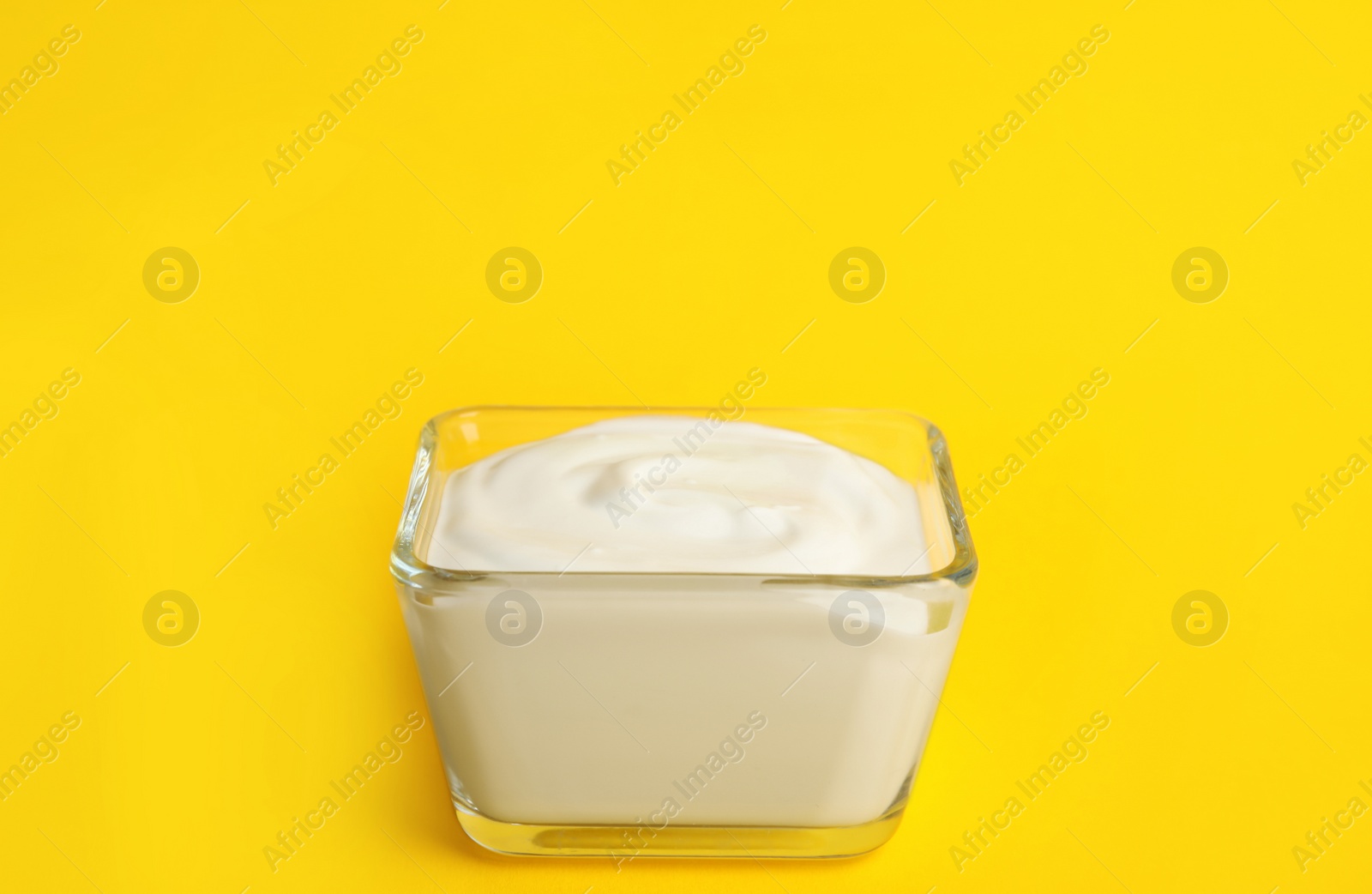 Photo of Tasty organic yogurt in glass bowl on yellow background