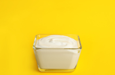 Photo of Tasty organic yogurt in glass bowl on yellow background