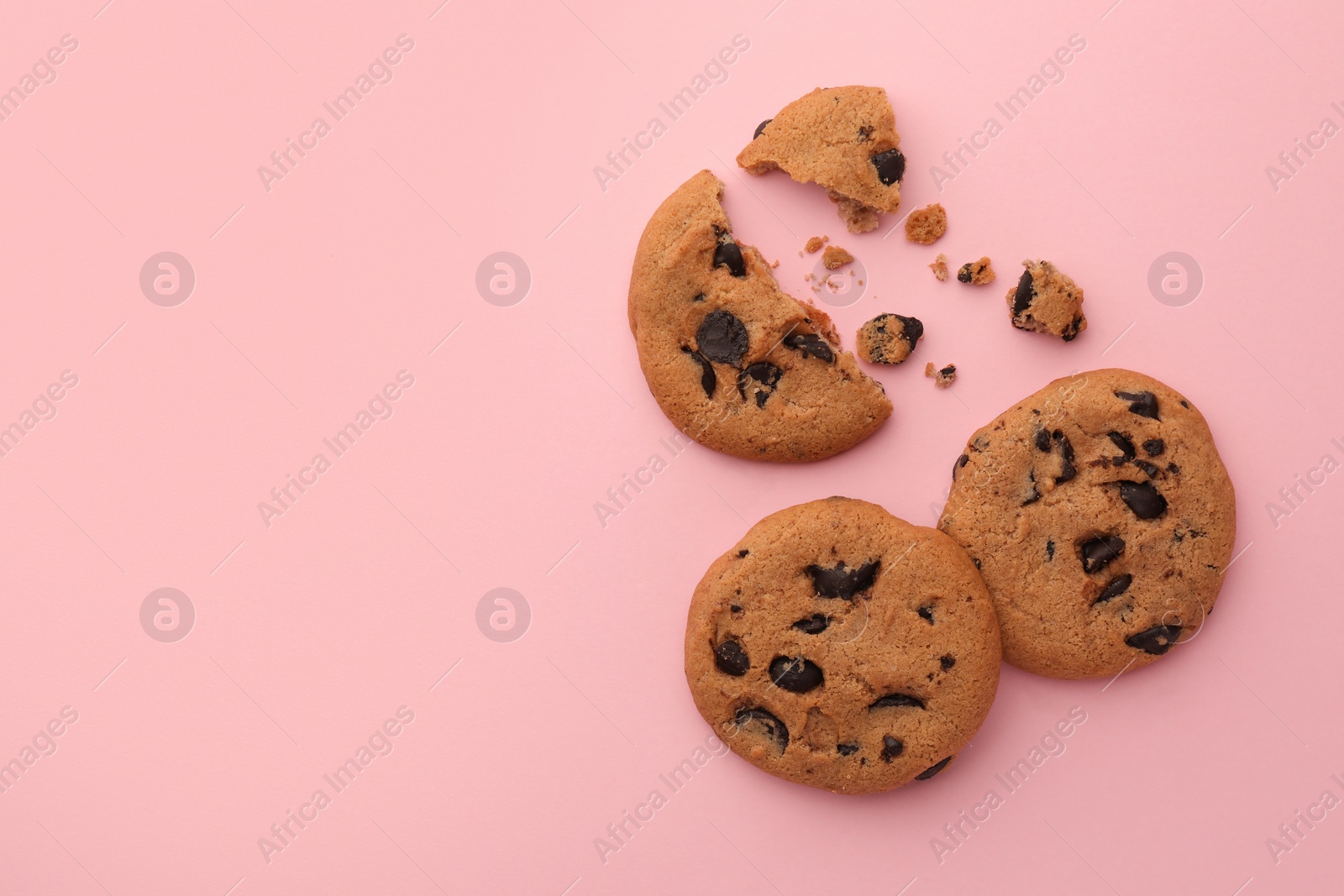 Photo of Many delicious chocolate chip cookies on pale pink background, flat lay. Space for text