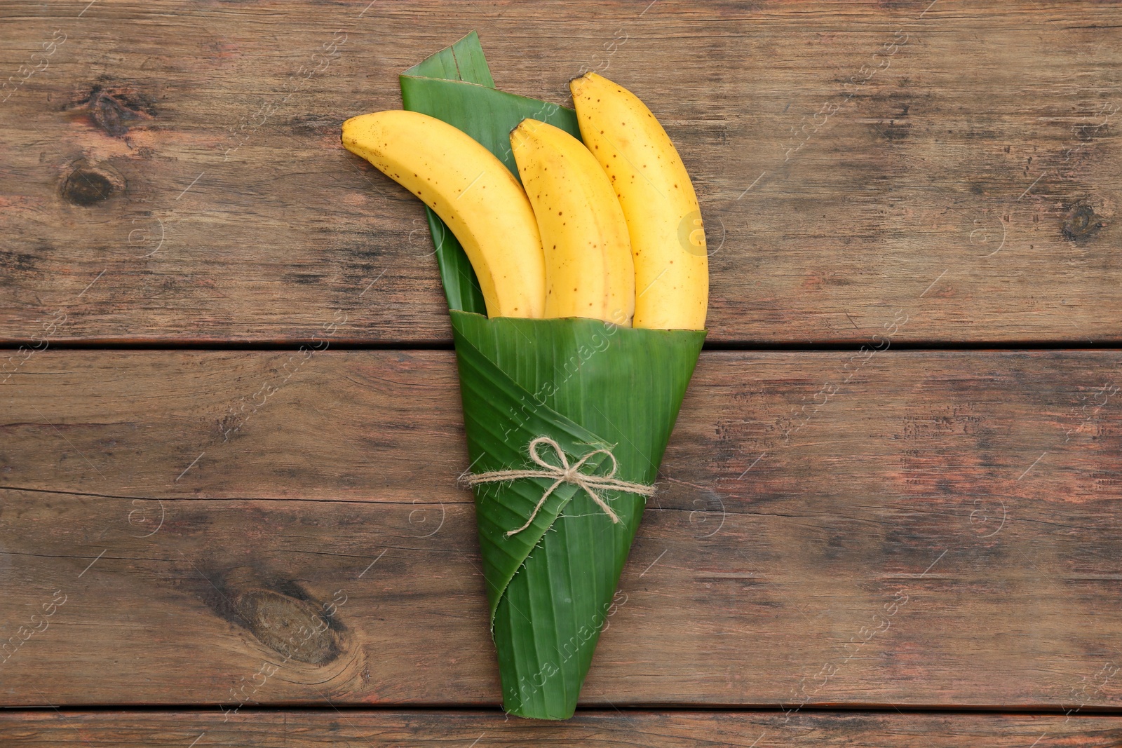 Photo of Delicious ripe bananas wrapped in fresh leaf on wooden table, top view