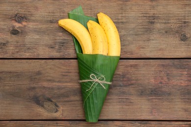 Delicious ripe bananas wrapped in fresh leaf on wooden table, top view