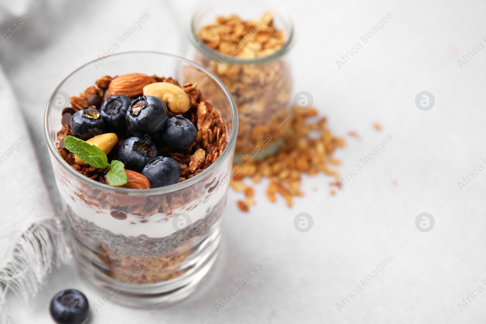 Photo of Tasty granola with berries, nuts, yogurt and chia seeds in glass on light table, closeup. Space for text