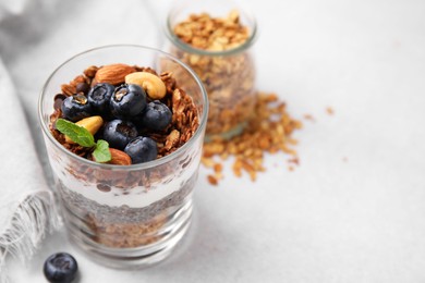 Photo of Tasty granola with berries, nuts, yogurt and chia seeds in glass on light table, closeup. Space for text