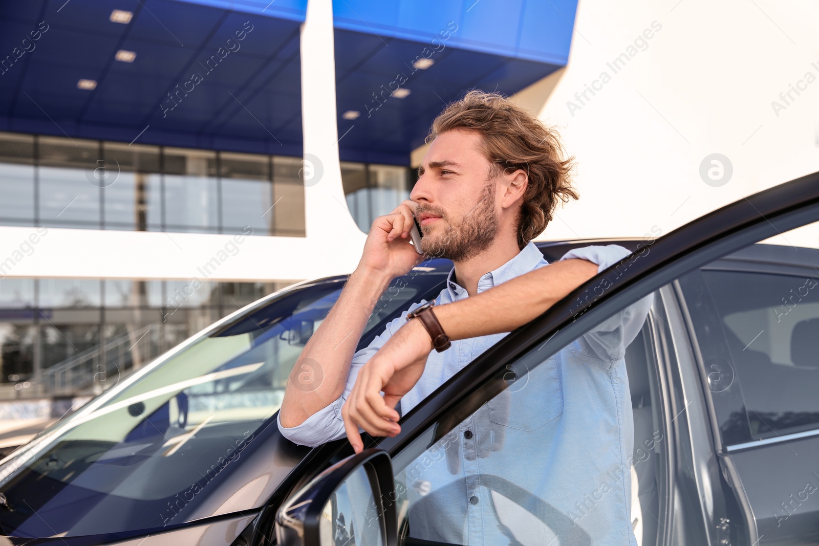 Photo of Young man talking on phone near modern car, outdoors