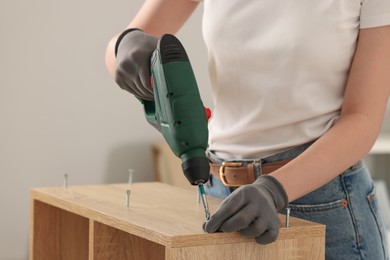 Photo of Woman with electric screwdriver assembling furniture indoors, closeup