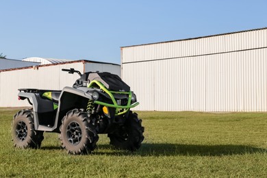 Modern quad bike in field near hangars on sunny day, space for text