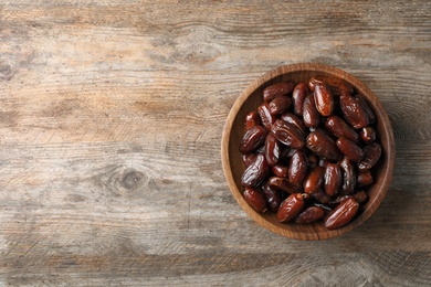 Photo of Bowl of sweet dates on wooden background, top view with space for text. Dried fruit as healthy snack