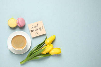 Photo of Delicious coffee, macarons, flowers and card with GOOD MORNING wish on light background, flat lay. Space for text