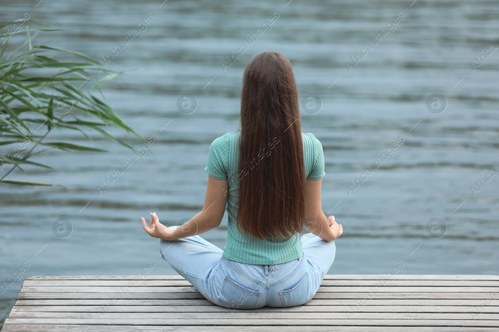 Photo of Teenage girl meditating near river, back view