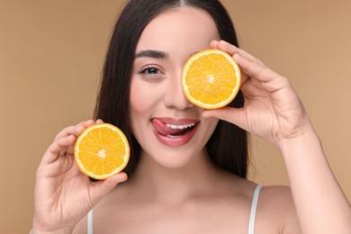 Beautiful young woman with pieces of orange on beige background