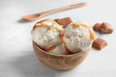 Delicious ice cream with caramel candies in bowl on white wooden table