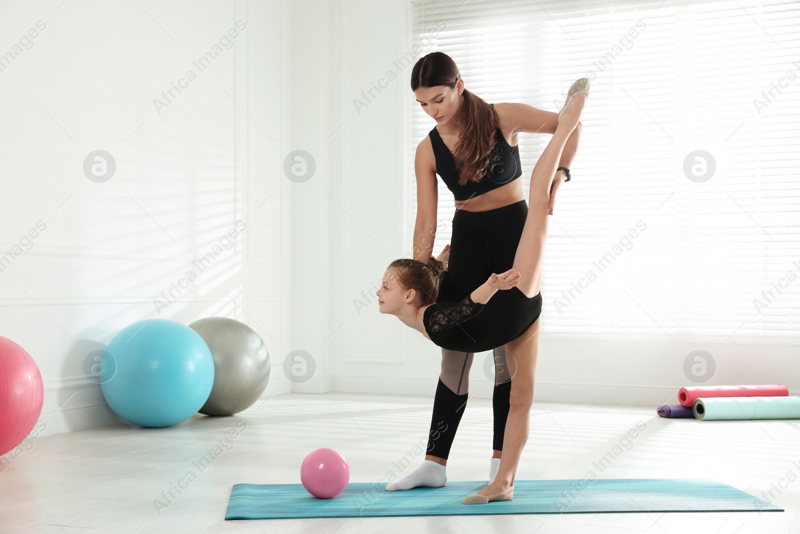 Photo of Gymnastic coach helping little girl to do standing split indoors