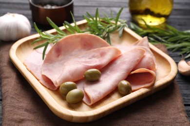 Photo of Slices of delicious ham with rosemary and olives on table, closeup