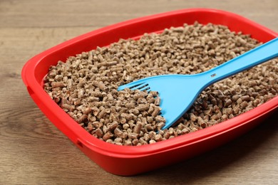 Cat litter tray with filler and scoop on wooden floor, closeup