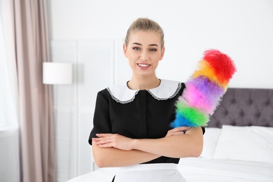 Photo of Young chambermaid with dust brush in bedroom