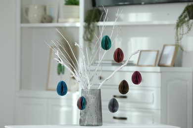 Branches with paper eggs in vase on white table indoors. Beautiful Easter decor