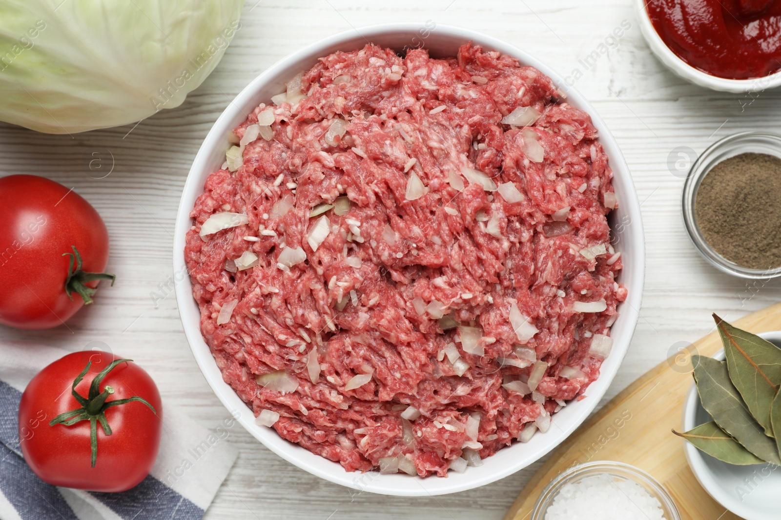 Photo of Meat filling in bowl and other ingredients for stuffed cabbage rolls on white wooden table, flat lay