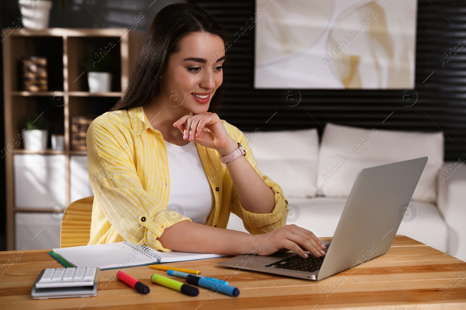 Photo of Young woman watching webinar at table in room