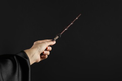 Photo of Wizard holding magic wand on black background, closeup. Space for text