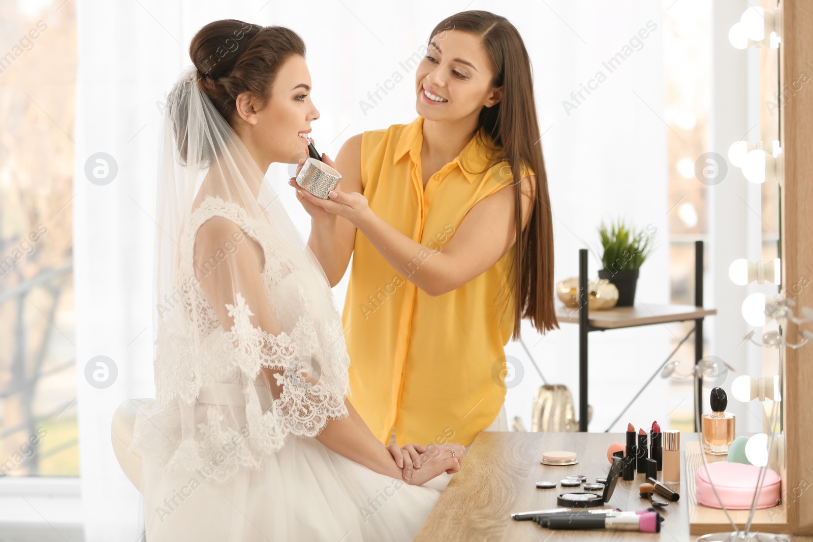 Photo of Makeup artist preparing bride before her wedding in room