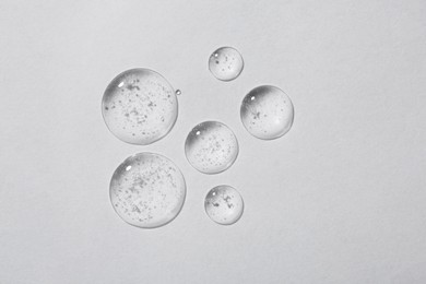 Photo of Drops of cosmetic serum on white background, top view