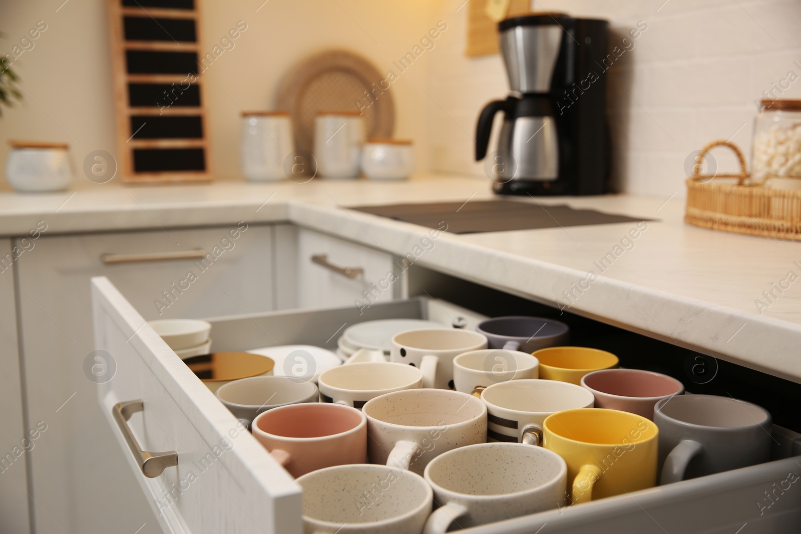 Photo of Open drawer with cups and coffeemaker on countertop in kitchen