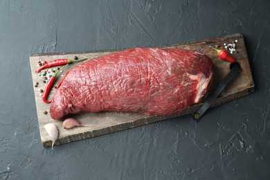 Photo of Piece of raw beef meat, garlic, chili and spices on grey textured table, top view