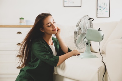 Photo of Woman enjoying air flow from fan at home. Summer heat