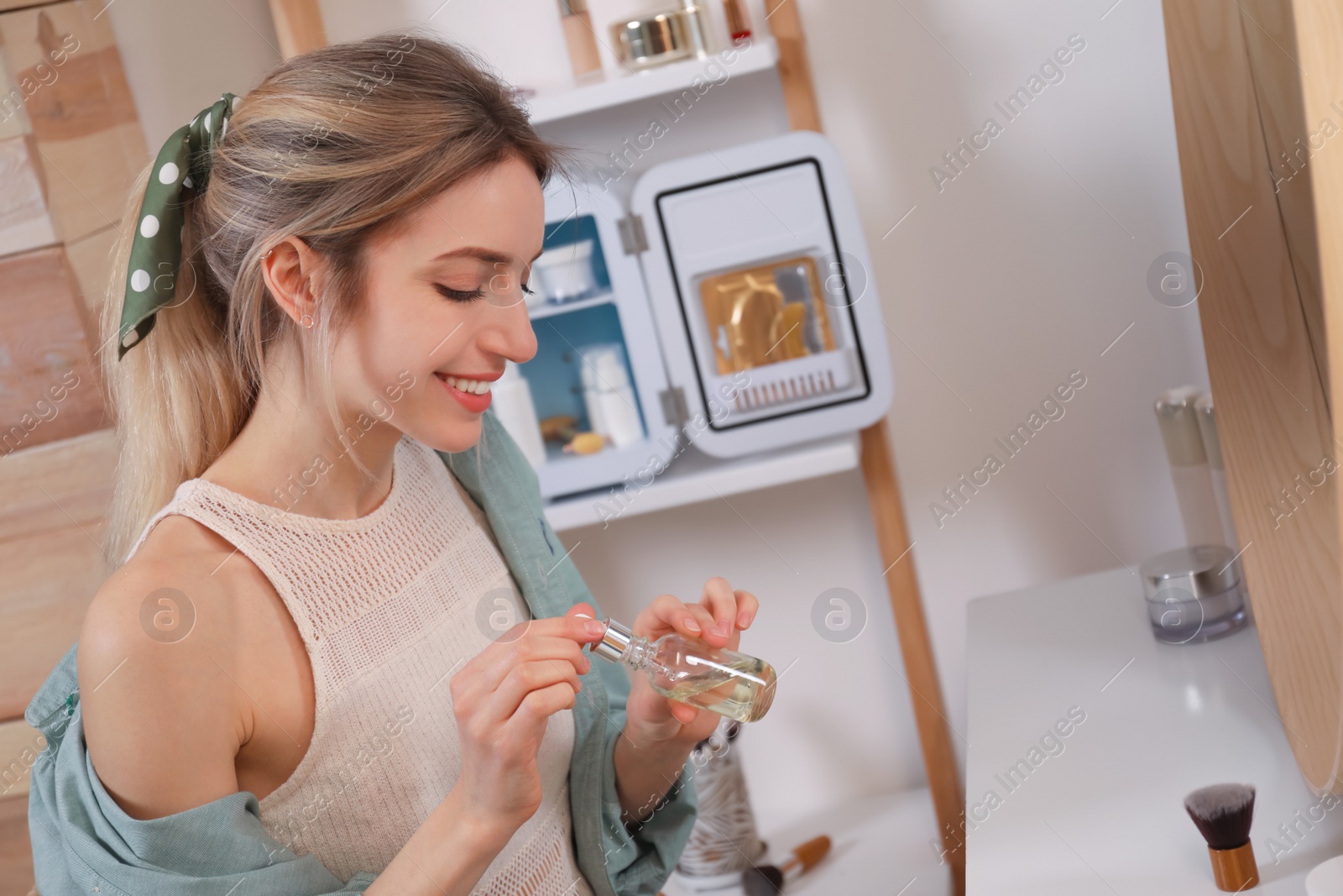 Photo of Woman using cosmetic product near mini fridge indoors