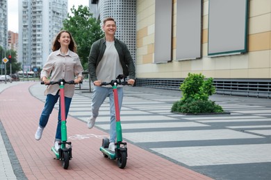Photo of Happy couple riding modern electric kick scooters on city street, space for text
