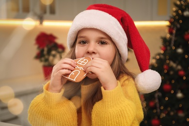 Photo of Cute little girl with Christmas gingerbread cookie at home