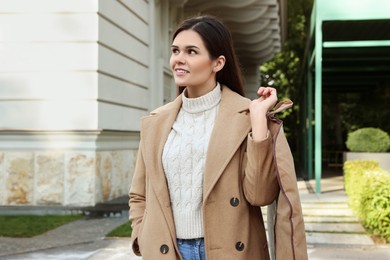 Photo of Attractive happy woman holding garment cover with clothes outdoors. Dry cleaning service