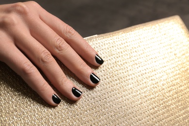 Photo of Woman with black manicure holding clutch, closeup. Nail polish trends