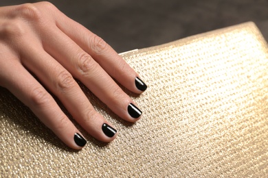 Woman with black manicure holding clutch, closeup. Nail polish trends