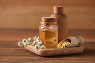 Photo of Bottles of chamomile essential oil and flowers on wooden table