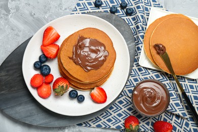 Photo of Tasty pancakes with chocolate paste and berries served on grey table, flat lay