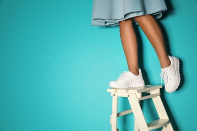 Photo of Woman in stylish sneakers on ladder near color wall, closeup. Space for text