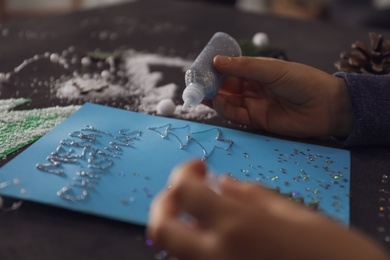 Photo of Little child making Christmas card at table, closeup