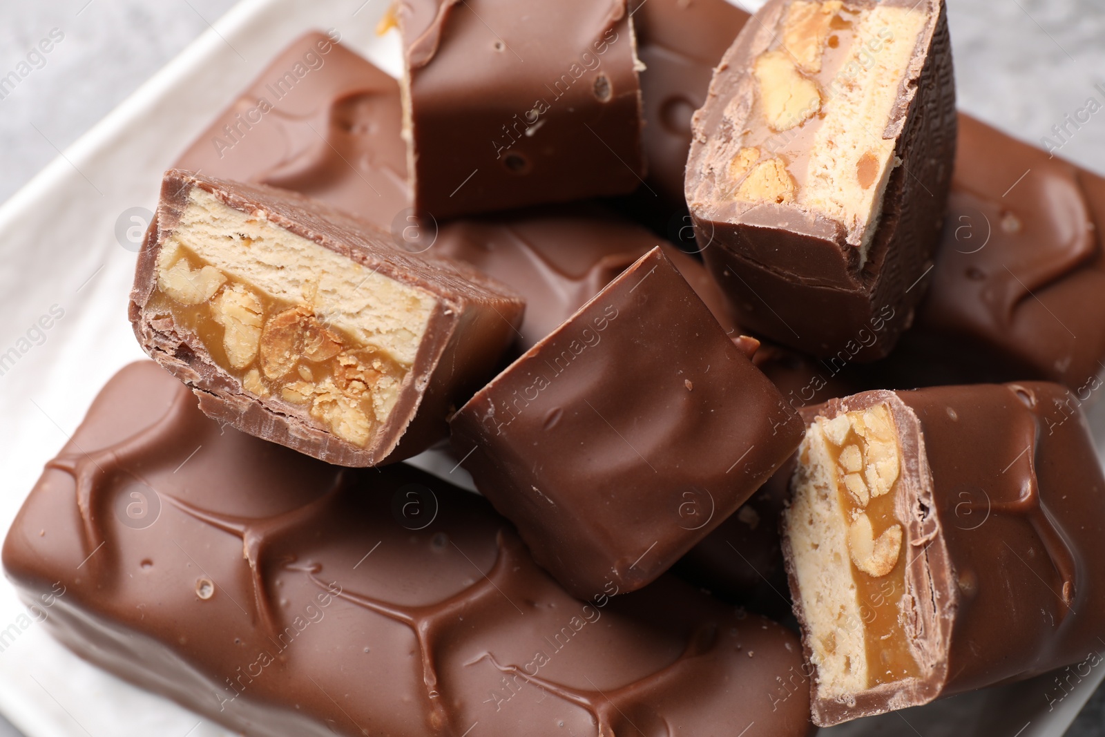Photo of Tasty chocolate bars with nougat, caramel and nuts on plate, closeup